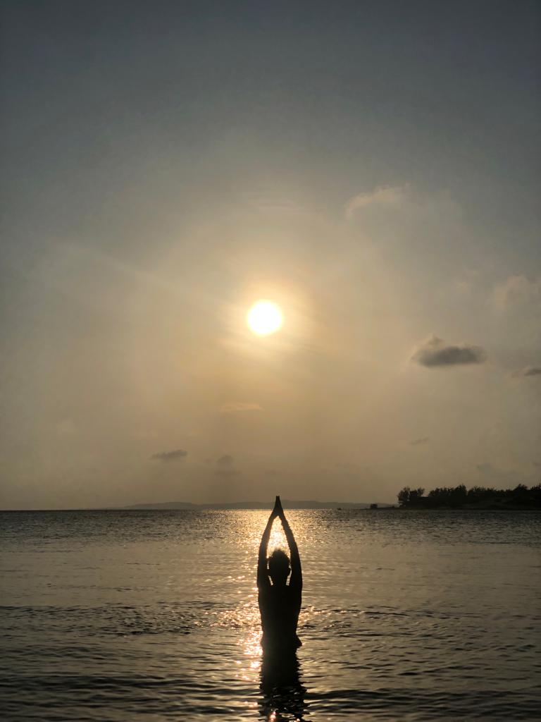 a woman doing yoga infront of the ocean at sunset